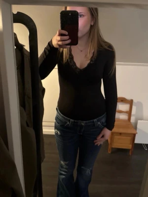 Svart långärmad body med spets - Svart långärmad body med v-ringning och snygga spetsdetaljer runt halsen. Sitter tight och har en stilren look som passar perfekt till jeans eller kjol. 