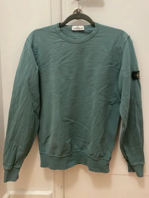 Turkos sweatshirt från Stone Island - Snygg turkos sweatshirt från Stone Island junior. Passar storlek 160-170 cl. Första bilden mest rättvisande i färgen. En mycket diskret vit fläck på framsidan som syns i ljus (se bild 2), går möjligtvis att tvätta bort och tyget något uppruggat vid ett ställe på baksidan (se sista bilden). Ingen av defekterna är något man tänker på.