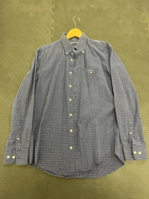 GANT skjorta  - Klassisk blårutig skjorta från Gant med button-down krage och bröstficka. Skjortan har vita knappar och lång ärm, perfekt för en stilren och avslappnad look. Tillverkad i mjuk bomull som känns skön mot huden.