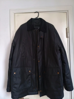 Oljejacka - Klassisk svart oljejacka från lager 157, modell HUNT. Jackan har stora framfickor med tryckknappar, ståkrage och dragkedja med knappslå. Materialet är tåligt och vattenavvisande, perfekt för kyligare dagar. Enkel och stilren design som passar till många outfits.