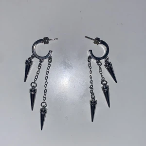 Silvriga örhängen med kedjor och spikes - Säljer ett par coola silvriga örhängen med ringformad bas och tre hängande kedjor på varje örhänge, dekorerade med spetsiga spikes. Perfekta för dig som gillar en edgy och alternativ stil. Metallisk finish och trendig design.