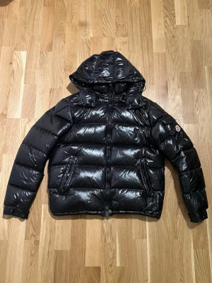 Svart Moncler Jacka - Säljer en svart, glansig pufferjacka från Moncler. Jackan är i storlek S och nyskick, inga tecken på använd. Väldigt bekväm och varm samt väldigt snygg, rekommenderar starkt. Hör av dig vid intresse/funderingar. PRIS KAN DISKUTERAS!