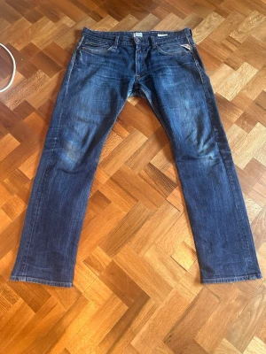 Blå archive jeans från replay  - Snygga blå jeans från replay med klassisk rak passform och fem fickor. Jeansen har slitningar och subtila tvättade detaljer som ger en cool, avslappnad look. Tillverkade i denim med tydliga sömmar och patch bak i midjan. Står w36 men skulle säga att de är w33-34 