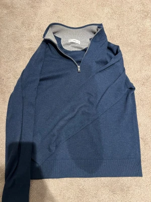 Marinblå stickad tröja med half zip MNG - Snygg marinblå stickad tröja från MNG i storlek S. Tröjan har en stilren half zip-dragkedja vid halsen och ribbade muddar. Perfekt för dig som gillar enkel och clean stil. Materialet är mjukt och skönt mot huden.