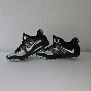 Nike KD svartvita sneakers - Snygga Nike KD sneakers i svart och vitt med coola detaljer och mönstrad sula. Skorna har en låg silhuett, mesh-ovandel och tydlig Nike swoosh i vitt på sidan. Perfekta för dig som gillar basketstil och streetwear.