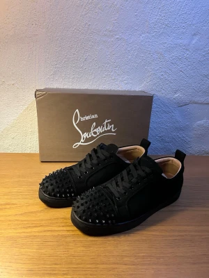 Christian Louboutin skor  - Snygga svarta sneakers från Christian Louboutin med mattsvarta nitar över tån. Skorna har en låg siluett, ovandel i mocka och klassisk röd sula. Insidan är beige Det är storlek 42,5 så om du hat 42 eller 43 så kommer dom passa för dom är bra i storleken… mvh Rasmus 