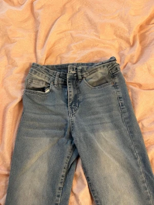 Blå jeans med dekorerade bakfickor - Säljer ett par blå jeans med snyggt slitna detaljer och dekorerade bakfickor med silverfärgade knappar och mönstrad söm. Klassisk femficksmodell och rak passform. Perfekta för dig som gillar en cool och avslappnad stil. Där bak är det ett litet hål då ”bält fästet” gått av. Passar en xs/s (jag har s i byxor och de passar mig i midja)