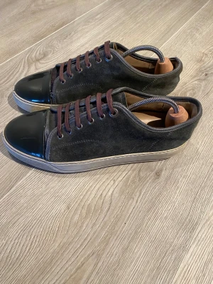 Svarta sneakers med mocka och lack - Stilrena svarta/bruna lanvins med ovandel i mocka och tåparti i blankt lack. Skorna har bruna skosnören och en vit sula med diskret textur. Perfekta för dig som gillar en clean och modern look med lite edge. Som ni ser på sista bilden har de hål i sulan och därav priset. De är storlek 42 men passar mer 43. Om ni har några frågor är det bara att skriva!