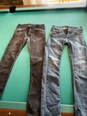 Två par Lee-jeans  - Säljer två par jeans, ett par klassiska blå Lee-jeans och ett par svarta Lee-jeans. Bra skick på båda och passar till mycket. Dom blåa har en storlek på 28/32 och dom svarta en storlek på 32/34. 