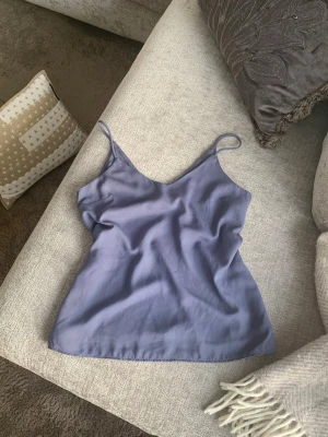 Ljuslila linnetopp med smala band - Säljer en stilren ljuslila linnetopp med tunna axelband och v-ringad hals. Toppen har en enkel och avslappnad passform, perfekt för varma dagar. Materialet känns lätt och svalt mot huden.