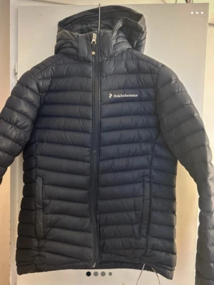 Svart pufferjacka Peak Performance - Svart pufferjacka från Peak Performance med huva och dragkedja framtill. Jackan har broderad logga på bröstet och R&D-märke på ärmen. Quiltad design och lätt vadderad, perfekt för kalla vinterdagar. Har it kommit till nytta. Skriv för mer information💞