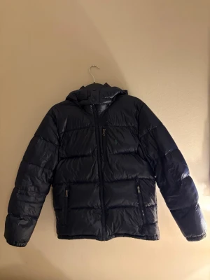 Mörkblå pufferjacka från Polo Ralph Lauren - Snygg mörkblå pufferjacka från Polo Ralph Lauren med huva och dragkedja framtill. Jackan är helt i nyskick och som sprillans ny. Skriv för fler funderingar eller frågor! Priset är inte spikat i sten! Storleken är 18-20 år men passar en person som är runt cirka 168-175.
