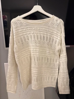 Vit virkad stickad tröja - Säljer en vit stickad tröja med virkat mönster och rund hals. Tröjan har långa ärmar och ett luftigt, detaljerat mönster som ger en cool och avslappnad vibe.