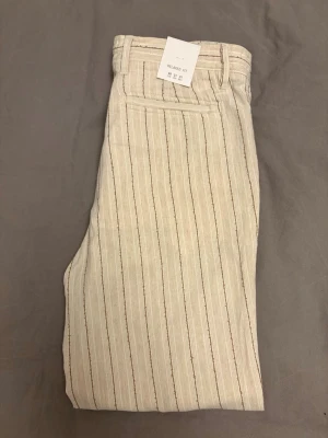 Zara Men linnebyxor relaxed fit oanvända  - Säljer ett par beige linnebyxor med ränder, relaxed fit. Materialet är luftigt linneblandat tyg. Säljer pga för småa. Alla taggar och prislappar sitter kvar. Pris hos Zara 559kr. Sitter som ett par M byxor