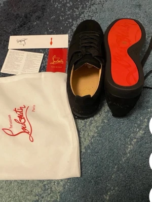 Svarta sneakers från Christian Louboutin - Snygga svarta sneakers från Christian Louboutin med klassisk röd sula och diskret logga. Skorna är låga och har ovandel i mocka och läder, samt svarta skosnören. Perfekta för dig som vill ha en exklusiv och stilren look.