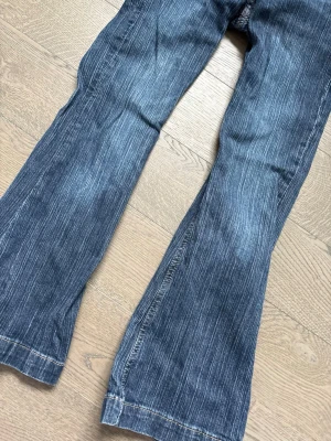 Blå bootcut jeans med slitningar - Säljer ett par blå bootcut jeans med snygga slitningar och detaljer. Jeansen har klassisk femficksdesign och vida ben🌟🌟 storlek 10-12