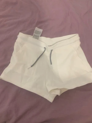 Vita shorts med snörning - Snygga vita shorts med blåvit snörning i midjan och två fickor framtill. Perfekta för varma dagar och har en avslappnad passform. Tillverkade i mjuk bomull för extra komfort.