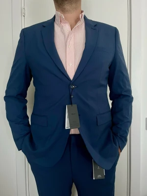 Marinblå kostym blazer från Mango men, storlek 54 - Snygg marinblå  kostym blazer från Mango men, slim fit 54 med klassisk passform. Kavajen har två knappar, smala slag och fickor med lock.  Materialet är slätt och stilrent, perfekt för en dressad look.