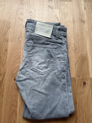Grå jeans från Jacob Cohen - Snygga ljusgrå jeans från Jacob Cohen med klassisk femficksdesign och diskret logopatch bak. Jeansen har raka ben och är perfekta för dig som gillar stilrena och moderna jeans.