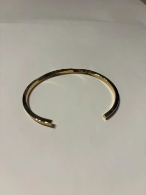 Guldigt minimalistiskt armband - Snyggt och stilrent armband i metall med guldfinish. Armbandet har en öppen design och är lätt att justera runt handleden. Perfekt för dig som gillar enkel och modern stil. Passar till många olika looks och är lätt att matcha med andra smycken. Säljer då det inte kommer till användning 