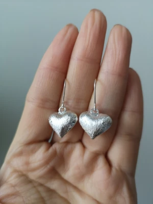 Silvriga hjärtformade örhängen - Säljer ett par snygga örhängen i silverfärg med hjärtformad design. De har en matt, lite borstad yta och hängs på krok. Perfekta för dig som gillar stilrena accessoarer med en söt twist.