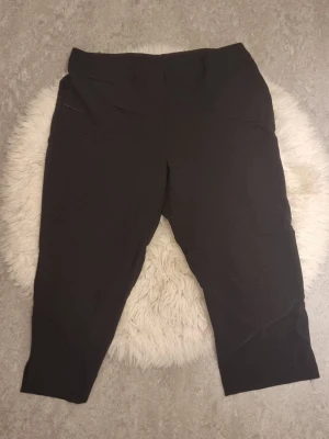 Svarta leggings från KappAhl - Säljer ett par klassiska svarta capris från KappAhl i storlek 46. De har en hög midja och är tillverkade i ett stretchigt material som sitter tight och bekvämt. Perfekta till både oversized tröjor och crop tops.