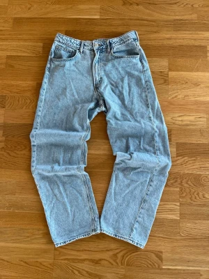 Ljusblå loose fit jeans från H&M - Säljer ett par ljusblå jeans från H&M med loose fit, justerbar midja och raka ben. Klassisk femficksmodell med snygga kontrastsömmar. Perfekta för en avslappnad och trendig look. Byxorna är i storlek 170/S. Skriv om du undrar något så löser vi det!
