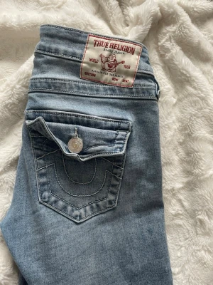 Ljusblå True Religion jeans - Säljer ett par ljusblå jeans från True Religion med klassisk kontrastsöm och ikonisk fickdetalj med knapp. Jeansen har en slim fit-modell och är tillverkade i mjukt denimtyg. Perfekta för dig som gillar streetwear och vill ha en snygg, avslappnad look. har inget fast pris så BUDA,