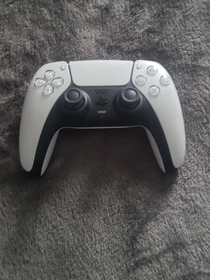 Vit PlayStation 5 DualSense handkontroll - Säljer en vit PlayStation 5 DualSense handkontroll från Sony. Den har en modern design med svart mittparti, touchpad och klassiska PlayStation-knappar. Ergonomisk form och tillverkad i plast, perfekt för gaming.