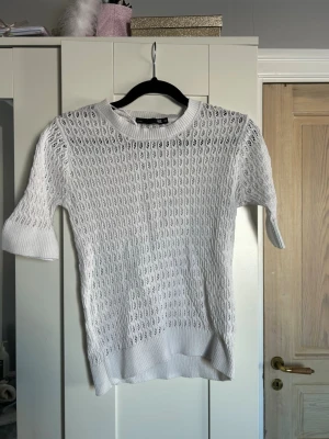 Vit stickad topp med hålmönster - Säljer en vit stickad topp med korta ärmar och snyggt hålmönster. Använd nån enstaka gång, säljer då jag inte får användning av den