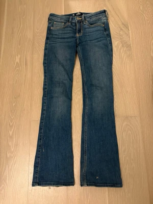 Blå bootcut jeans från Hollister - Snygga blå bootcut jeans från Hollister med låg midja. Jeansen har en lätt utsvängd passform nertill och detaljerade sömmar. Perfekta för en avslappnad och trendig look. 