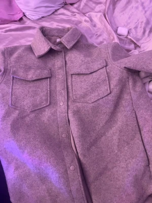 Beige overshirt med fickor - Säljer en beige overshirt jacka i mjukt, filtliknande material. Jackan har två stora bröstfickor med lock, klassisk krage och tryckknappar framtill. Perfekt för lager på lager och en avslappnad streetstil.