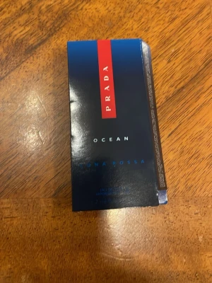 Prada Luna Rossa Ocean parfymprov - Snyggt parfymprov från Prada Luna Rossa Ocean. Förpackningen är mörkblå med en röd detalj och vit text. Provet kommer i en liten genomskinlig plastflaska med sprayfunktion. Perfekt att ha med sig i väskan eller testa en ny doft.
