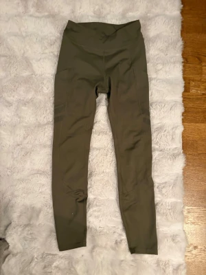 Olivgröna leggings från Stronger - Snygga olivgröna leggings från Stronger med hög midja och tight passform. Tillverkade i ett stretchigt material av 74% återvunnen polyester och 26% elastan. Perfekta för träning eller chill dagar. Designade i Sverige.