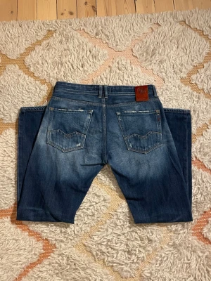 Blå Replay jeans med slitningar - Snygga replay jeans med slitningar i storlek W31 L30. Modellen är 187cm. Hör av dig vid minsta fundering