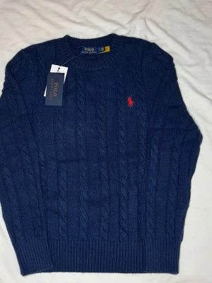 Mörkblå kabelstickad tröja Polo Ralph lauren💙 - Kabelstickad mörkblå tröja från Polo Ralph Lauren med rund halsringning och den klassiska röda logotypen broderad på bröstet. Tröjan har ribbade muddar vid ärmslut och nederkant. Perfekt för dig som gillar stilren och tidlös design. 💬skriv frågor 