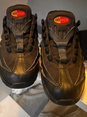 Svarta Nike Air Max 95 sneakers utan snören  - Säljer ett par svarta Nike Air Max 95 sneakers med röda detaljer och klassisk Air Max-logga på plösen. Skorna har en chunky sula, mesh och läderpaneler samt röda Swoosh på sidan. Perfekta för dig som gillar streetwear och vill ha en ikonisk look.