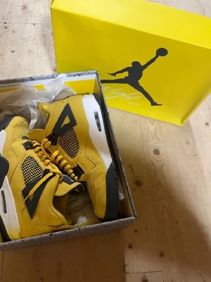 Air Jordan 4 Retro gul/svart - Säljer ett par Air Jordan 4 Retro sneakers i en riktigt fet gul färg med svarta detaljer och vit sula. Skorna har meshpaneler, klassiska plastdetaljer och synlig Air-enhet i hälen. Ovandelen är i mocka och de kommer i originalkartong.