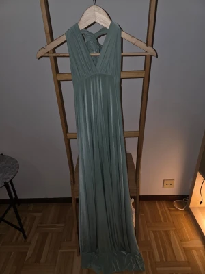 Ljusgrön långklänning med knyt - Snygg ljusgrön långklänning med breda axelband och knyt som man kan styla på mpnga olika sätt.. Klänningen har ett mjukt, fallande tyg och v-ringad front. Perfekt för dig som vill ha en elegant och enkel look. Klänningen passar mig som är XS/S meb har för vi den är onesize.