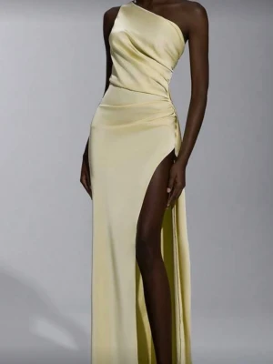Ljusgul oneshoulder långklänning - Elegant ljusgul långklänning i satinliknande material med oneshoulder-design och smal axelrem bak. Klänningen har hög slits på sidan och öppen rygg, vilket ger en riktigt snygg och modern look. Perfekt för dig som vill sticka ut.
