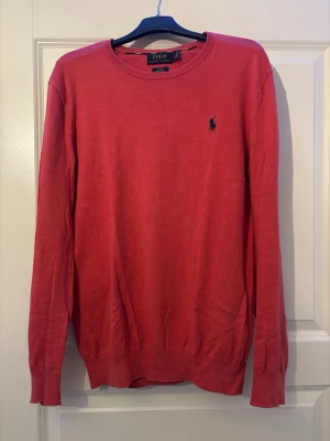 Röd tröja från Polo Ralph Lauren - Snygg röd långärmad tröja från Polo Ralph Lauren i slim fit-modell. Tillverkad i mjuk pima bomull och har den klassiska broderade loggan på bröstet. Rund halsringning och ribbade muddar vid ärmslut och nederkant.