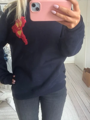 Mörkblå sweatshirt med rött märke - Säljer min blå sweatshirt med rött tryck som e as coolt. Älskar denna och den röda detaljen gör hela outfiten lite bättre!