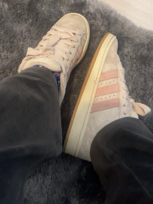 Adidas Campus ljusrosa sneakers - Säljer ett par Adidas Campus sneakers i ljusbeige mocka med klassiska tre rosa ränder på sidan och vit sula med gummidetalj. Skorna har lågt skaft och snörning framtill. Perfekta för dig som gillar en clean och stilren look. Helt ok skick.