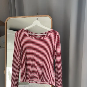 Randig långärmad tröja röd/vit - Säljer en långärmad tröja med smala röda och vita ränder. Tröjan har rund halsringning och är gjord i ett mjukt, stretchigt material som känns skönt mot huden. Perfekt för dig som gillar en enkel men snygg stil.