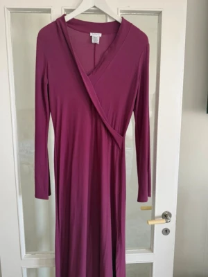 Lång vinröd omlottklänning Tehen - Snygg vinröd långklänning från Tehen med omlott-design och långa ärmar. Klänningen har en djup v-ringning och är tillverkad i ett mjukt, stretchigt material som ger en skön passform.