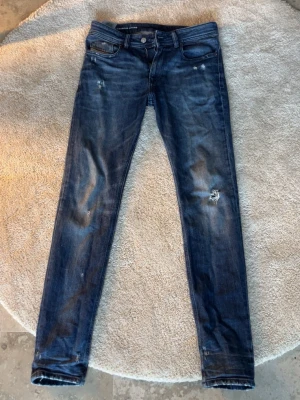Mörkblå slim jeans från Diesel - Säljer ett par mörkblå slim/skinny jeans från Diesel med slitningar och distressed detaljer på benen. Klassisk femficksmodell med låg midja och smal passform. Jeansen har snygga tvättade partier och är tillverkade i denim med stretch för extra komfort. Som nya kvalitetsmässigt