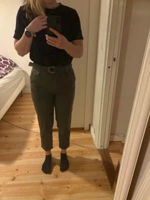 Bikbok Mörkgröna byxor i storlek XS - Säljer ett par mörkgröna chinos med hög midja och tillhörande bälte. Byxorna har avsmalnande ben och uppvikta benslut för en trendig look. Perfekta för dig som vill ha en stilren och bekväm byxa till vardags.