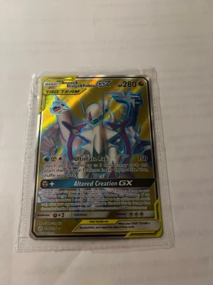 Pokémonkort Arceus & Dialga & Palkia GX - Säljer ett Pokémonkort med Arceus & Dialga & Palkia GX TAG TEAM. Kortet har en holografisk yta med guld och blå detaljer och är inplastat i ett skyddsfodral. Perfekt för samlare eller Pokémonfans som vill utöka sin samling.