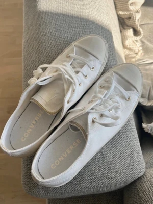 Vita låga Converse sneakers - Klassiska vita Converse sneakers i lågt snitt med vita snören och metallfärgade öljetter. Skorna är tillverkade i canvas och har en vit gummisula. Perfekta för en clean och stilren look. Lite mer sommar och lite tunnare i tyget. Köpt online men tyvärr för små för mig