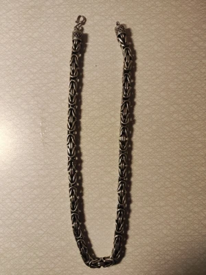 Kjejsarlänk 10mm tjock 55cm lång  - Säljer ett robust halsband i silver med flätad kedjedesign. Halsbandet har en unik, detaljerad struktur och kraftiga länkar som ger ett coolt och stilrent intryck. Perfekt för dig som gillar statement-smycken och vill sticka ut. Den e ganska tung! säljes enbart för att jag verkligen behöver pengarna! Nypris ca 18.000